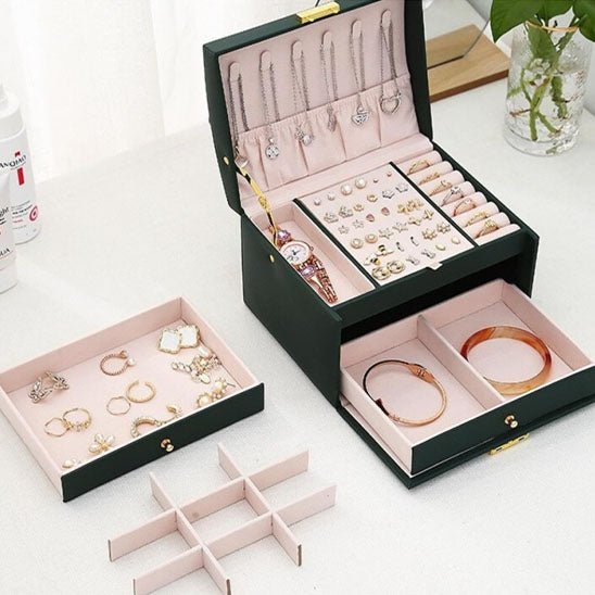 Boite-a-bijoux-prestige-rangement-innovant-vert-ouverte-remplie-de-bijoux-posée-sur-une-table-blanche