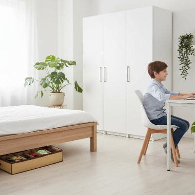 Rangement chaussures sous lit placé sur parquet sous côté latéral du lit dans une chambre d'un garçon travaillant sur son bureau