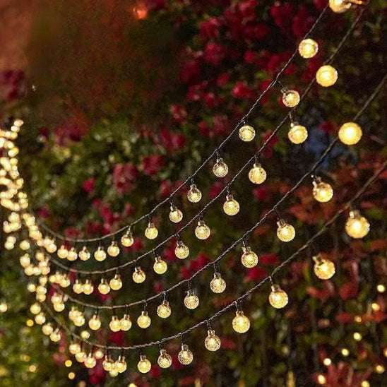 Guirlande solaire Luminéco lumière chaude allumée suspendue dessus rosiers décoration jardin 