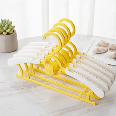 Cintre enfant jaune plusieurs groupés posés sur table blanche