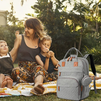 Sac à langer gris posé sur pelouse devant maman et bébés